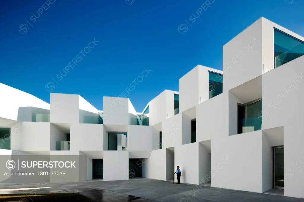 House for Elderly People, Alcaçer do Sal, Portugal. Architect: Francisco Aires Mateus Arquitectos, 2011. View of social housing complex in daylight with man in hat.