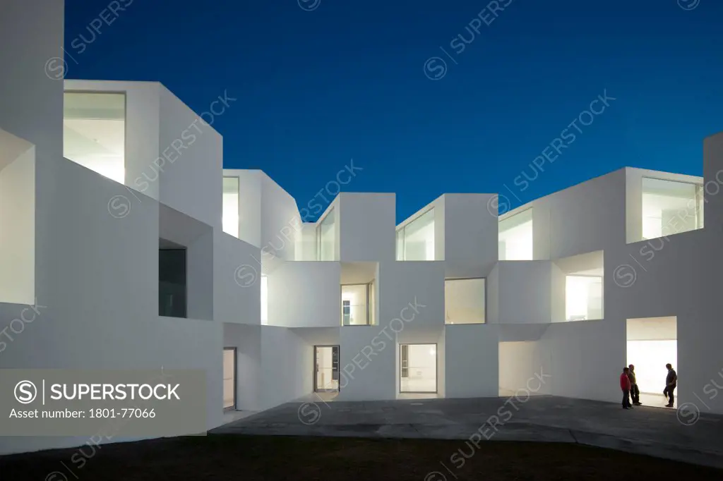 House for Elderly People, Alcaçer do Sal, Portugal. Architect: Francisco Aires Mateus Arquitectos, 2011. View of social housing complex at dusk with people.