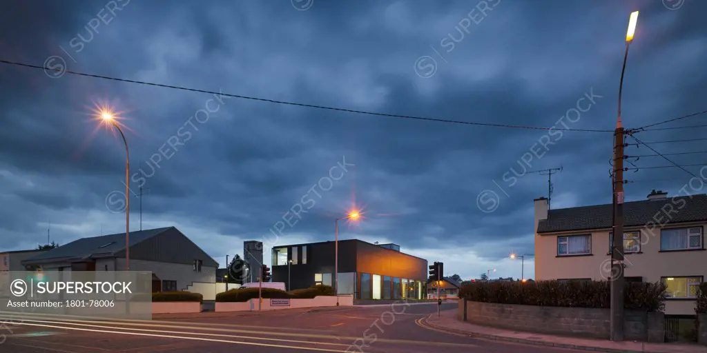 Claremorris Civic Offices, Public Offices, Europe, Ireland, Mayo, 2009, Simon J Kelly + Partners Architects. View of building from road showing black cladding, flush windows and surrounding buildings at dusk.