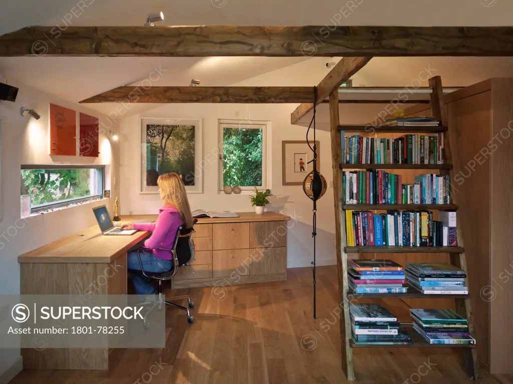 Garden Office, Berkhamsted, United Kingdom. Architect: SDP Design, 2012. Interior room view showing office desk, chair, bookcase, ladder and oak timber flooring with woman working at desks.