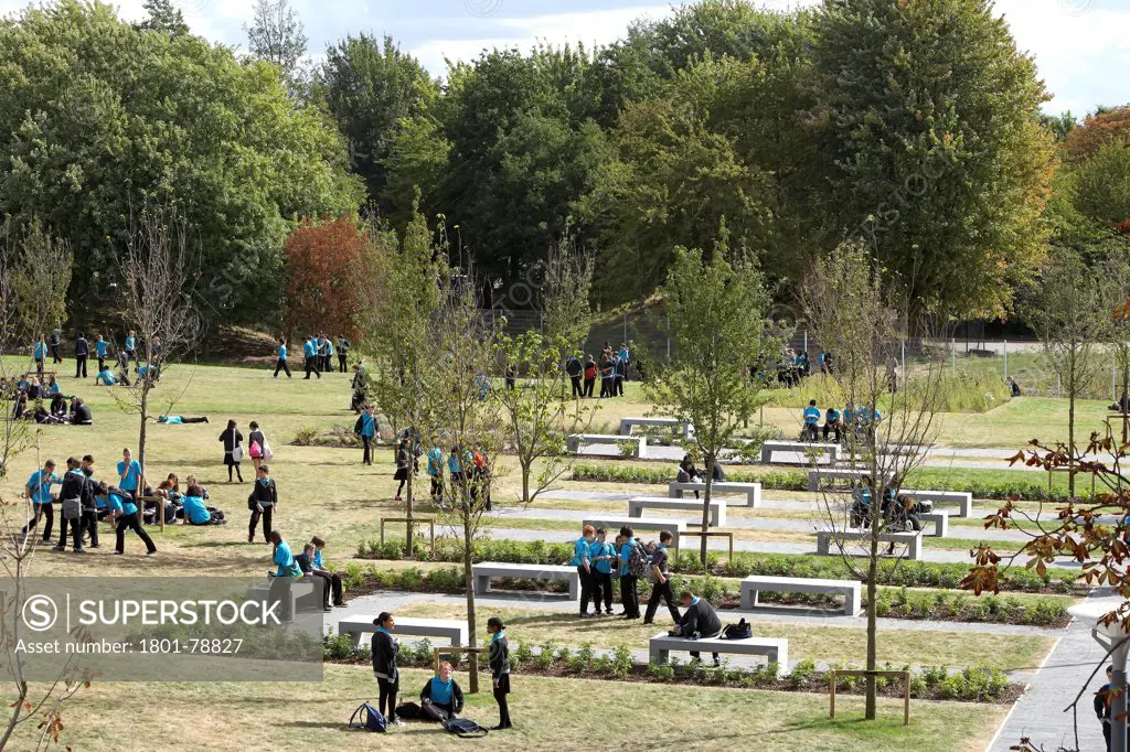 Thomas Tallis School, Greenwich, United Kingdom. Architect: John Mcaslan & Partners, 2012. Landscaped Green Grounds With Walkway And Students.