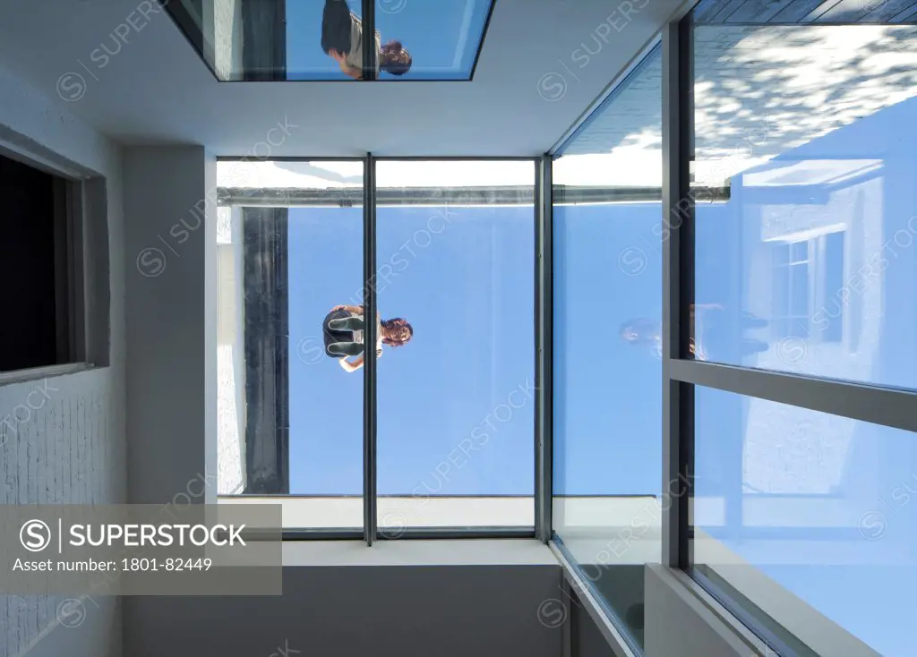 The Cut And Fold House, Twickenham, United Kingdom. Architect: Ashton Porter Architects, 2011. View looking up showing a woman standing on the glass extension demonstrating its strength.