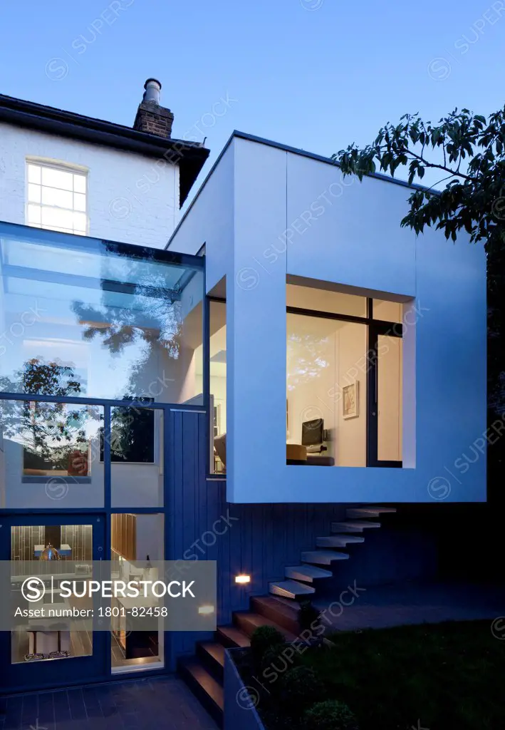 The Cut And Fold House, Twickenham, United Kingdom. Architect: Ashton Porter Architects, 2011. Rear elevation at dusk showing the extension illuminated from the living room area.