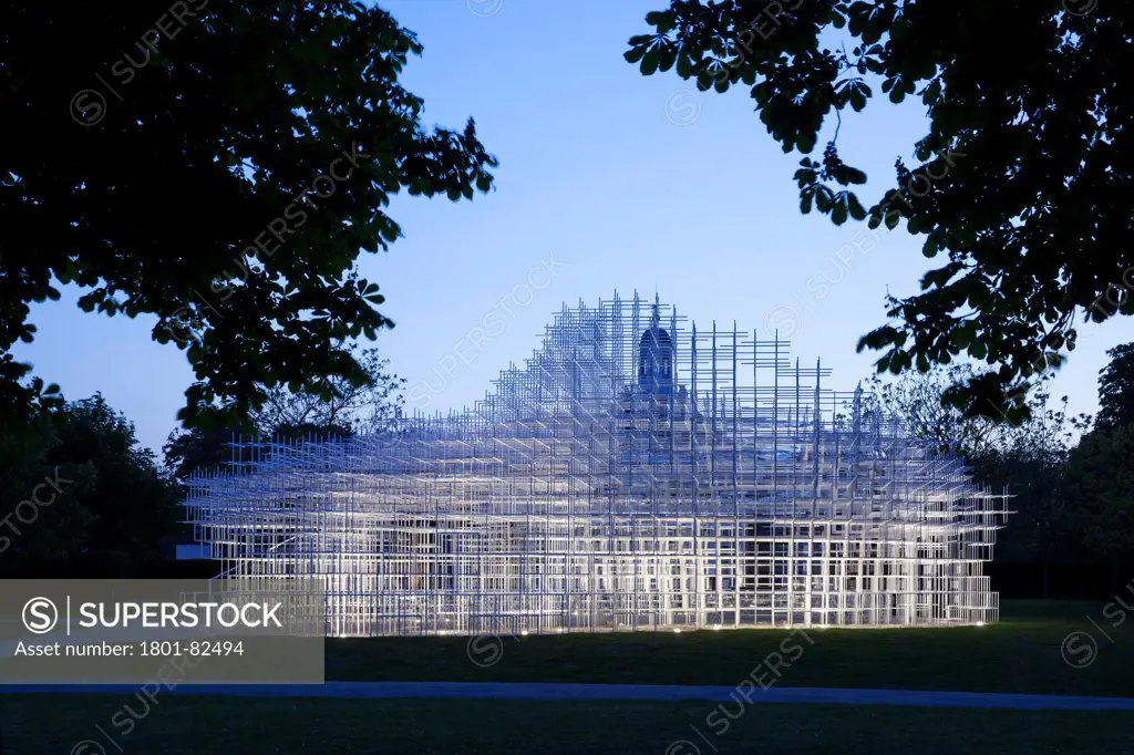 Serpentine Pavilion 2013, London, United Kingdom. Architect: Sou Fujimoto', 2013. General view looking west  through the trees in the park at dusk showing the glowing pavilion in context.