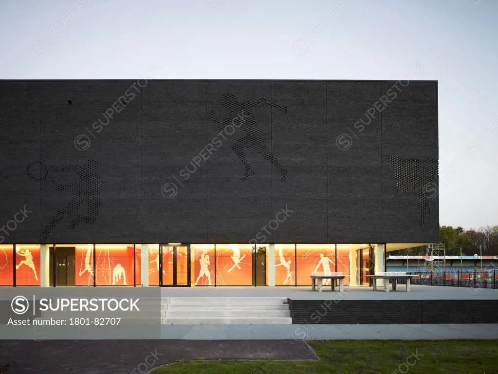 Fontys Sports College, Eindhoven, Netherlands. Architect: mecanoo architecten, 2012. Partial front elevation with glazed ground floor at dusk.