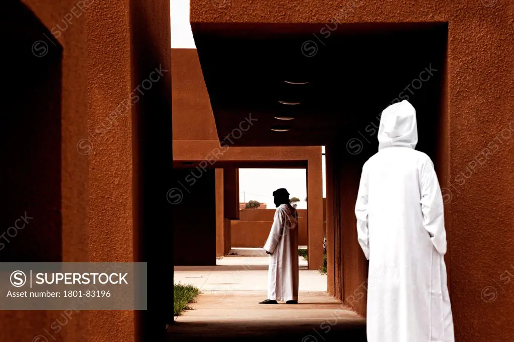 Technology School of Guelmim Morocco, Guelmim, Morocco. Architect: Saad El Kabbaj, Driss Kettani, Mohamed Amine Siana, 2011. Figures standing under canopied walkways.