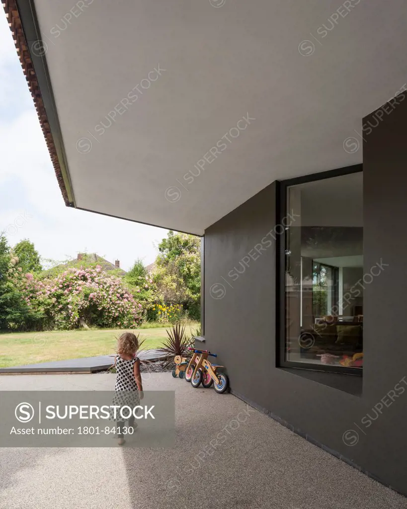 Wedge House, Surrey, United Kingdom. Architect SOUP Architects, 2013. View of entrance area with child walking towards bicycle.