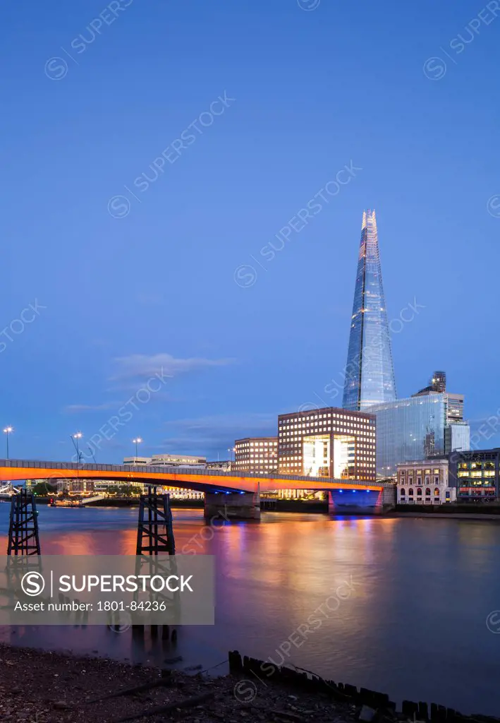 No.1 London Bridge, London, United Kingdom. Architect John S. Bonnington Partnership, 1986. View of the offices looking across the river Thameswith the Shard in the background and London bridge lit up in the foreground. Ancient river wharfs are visible at low tide to the bottom of the picture.