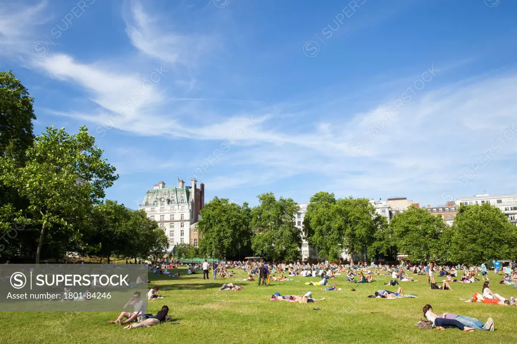 The Green Park, London, United Kingdom. Architect John Nash, 1820. View of Green Park looking east with the Ritz hotel in the background. Groups of people relaxing on a sunny Sunday having a picnic and sun bathing.