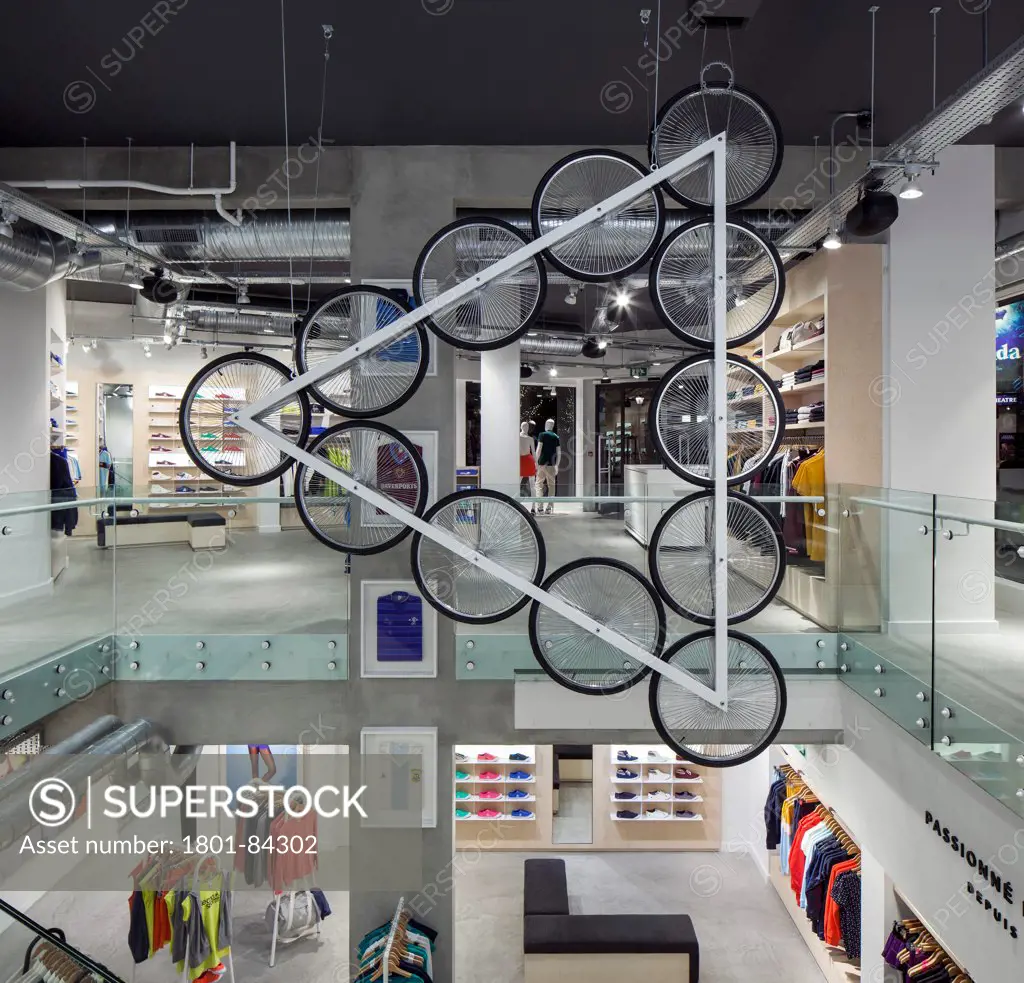 Le Coq Sportif London -FlagshipStore, London, United Kingdom. Architect Studio Oscar, 2013. Interior of the store showing the Kinetic Bicycle Sculpture hanging over the stairs, clothing and merchandise can be seen overtwo floors.