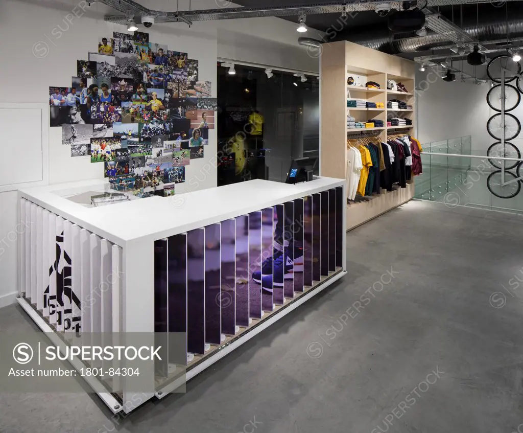 Le Coq Sportif London -FlagshipStore, London, United Kingdom. Architect Studio Oscar, 2013. Store counter and till with a rotating advertising board on the front and side merchandise in the background.