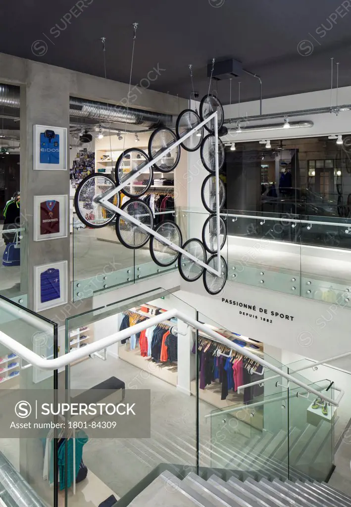 Le Coq Sportif London -FlagshipStore, London, United Kingdom. Architect Studio Oscar, 2013. Wide shot of the interior of the store showing the Kinetic Bicycle Sculpture hanging over the stairs, clothing and merchandise can be seen overtwo floors.