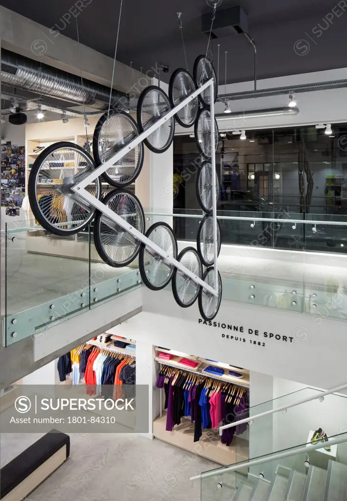Le Coq Sportif London -FlagshipStore, London, United Kingdom. Architect Studio Oscar, 2013. Interior of the store showing the Kinetic Bicycle Sculpture hanging over the stairs, clothing and merchandise can be seen overtwo floors.