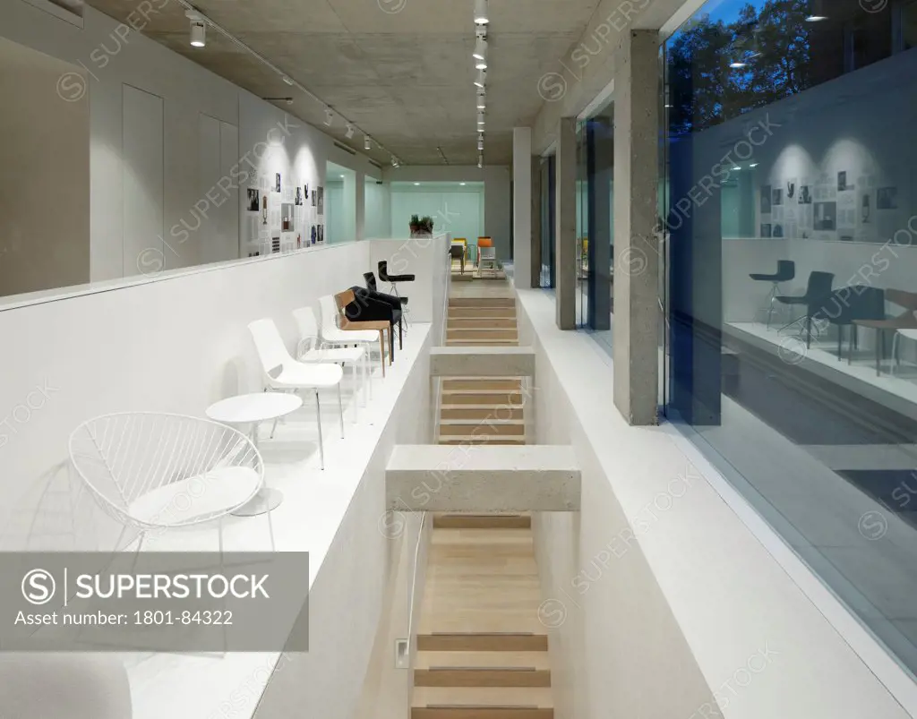 Arper London Showroom, London, United Kingdom. Architect 6A, 2012. View of stairs with white chair display running along the top large windows along the street with fine concrete columns.