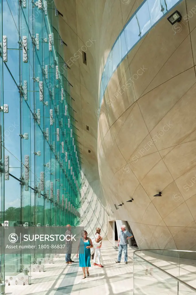Museum of History of Polish Jews, Warsaw, Poland. Architect Lahdelma & Mahlamaeki, 2013. A group of visitors walking round the back glass wall on a sunny afternoon.