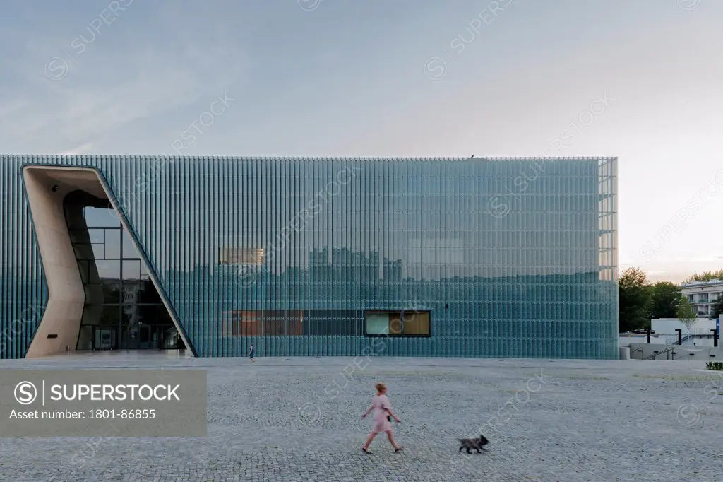 Museum of History of Polish Jews, Warsaw, Poland. Architect Lahdelma & Mahlamaeki, 2013. A woman walks her dog, in the square, a bird rests in the roof of the museum building.