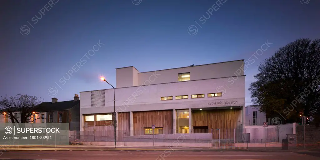 Scoil Mhuire Ogh, Dublin, Ireland. Architect Mary Laheen Architects, 2011. View of front facade from road taken one year after completion showing brick and timber detailing with interior lighting.