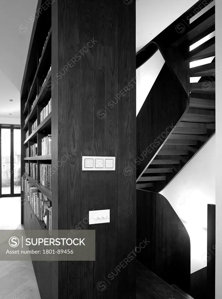 St Johns' Orchard, London, United Kingdom. Architect: John Smart Architects, 2013. Black and white  Interior View showing bookshelves with staircase in background.