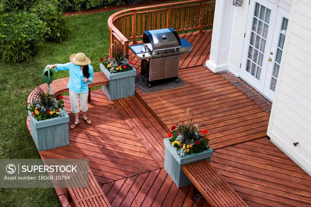 Woman watering flowers by BBQ with wooden benches and wood paneled floor in the backyard, Miami, USA. 03/24/2005