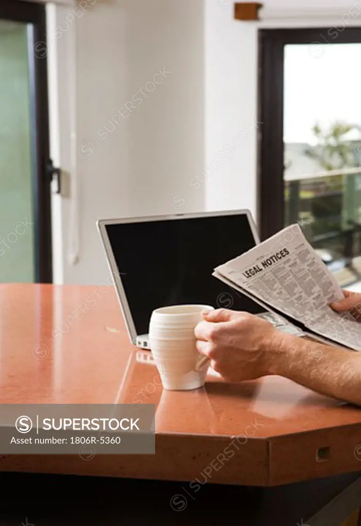 Man Reading Newspaper with Laptop and Coffee