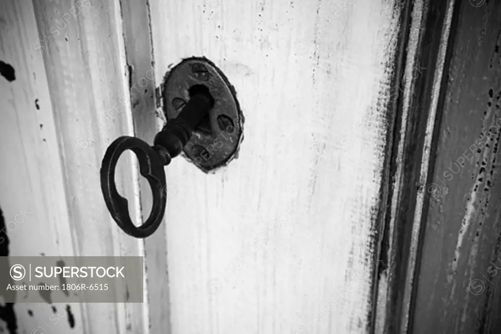 Black and white image of aged key in keyhole.