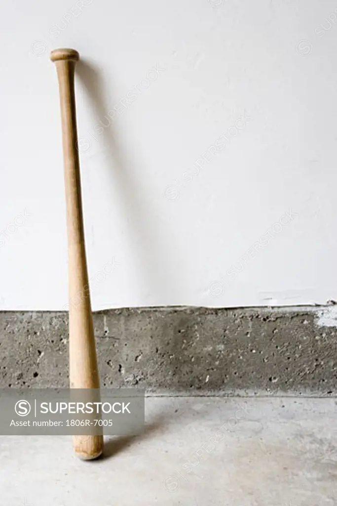 Detail of wooden baseball bat against white and concrete wall.