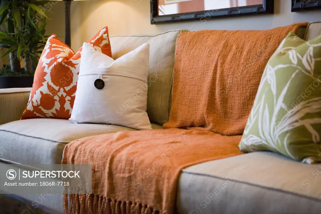 Comfortable sofa with orange throw blanket and decorative pillows