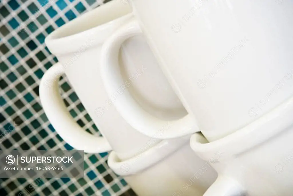 Stacked white coffee mugs in front of tile backsplash