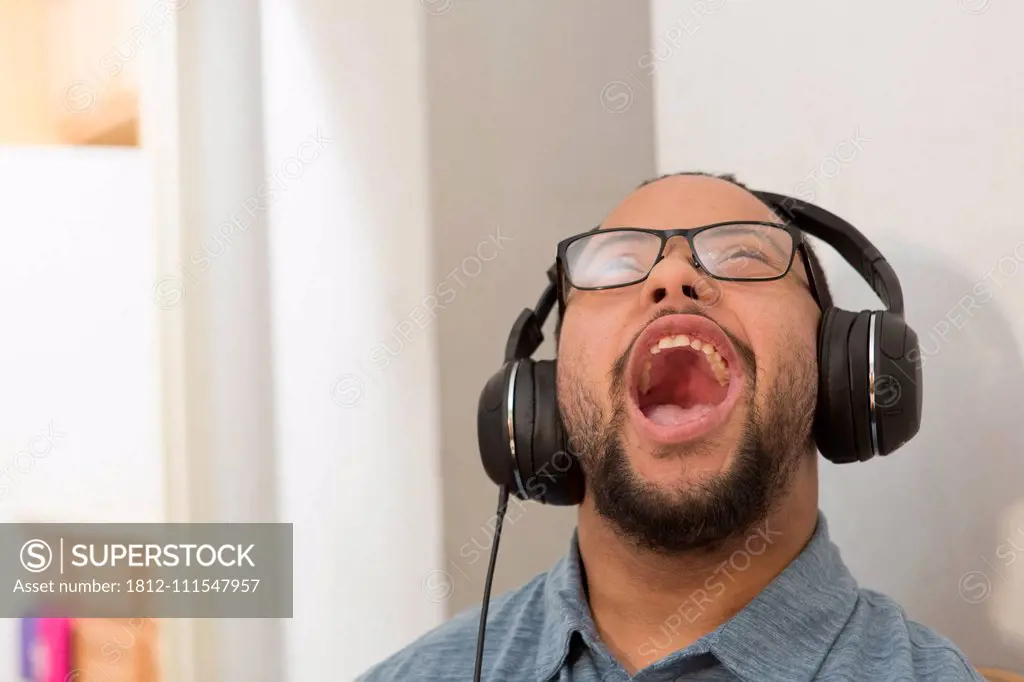 Happy African American man with Down Syndrome listening to music and singing with headphones at home