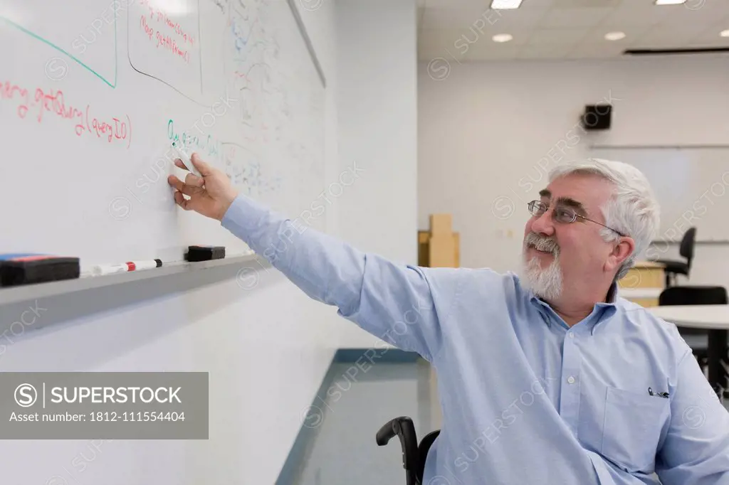 University professor with Muscular Dystrophy writing on a whiteboard in a classroom