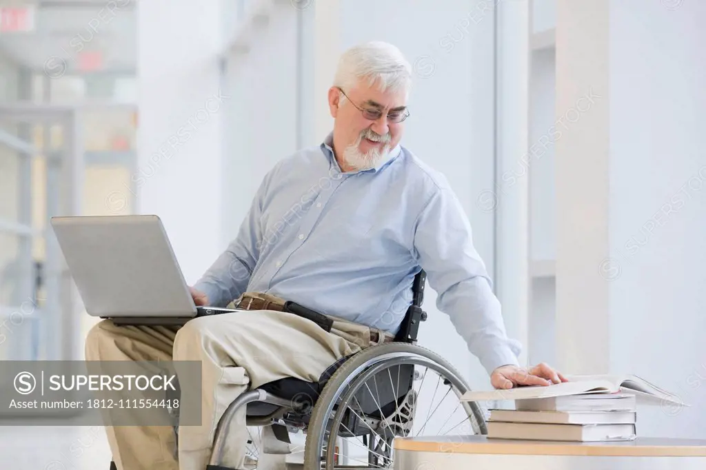 University professor with Muscular Dystrophy reading a book and using a laptop