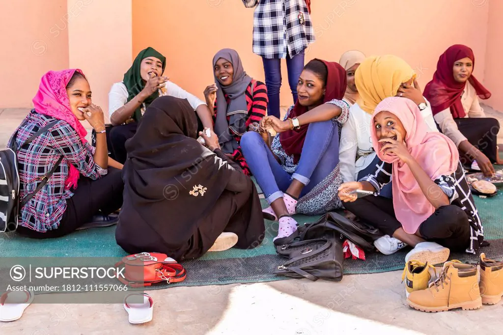 Young Sudanese women sitting on the ground visiting and eating together; Kerma, Northern State, Sudan