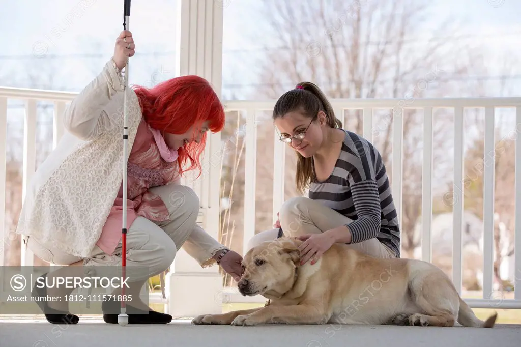 Two women with visual impairments, one with a service dog and one with a cane