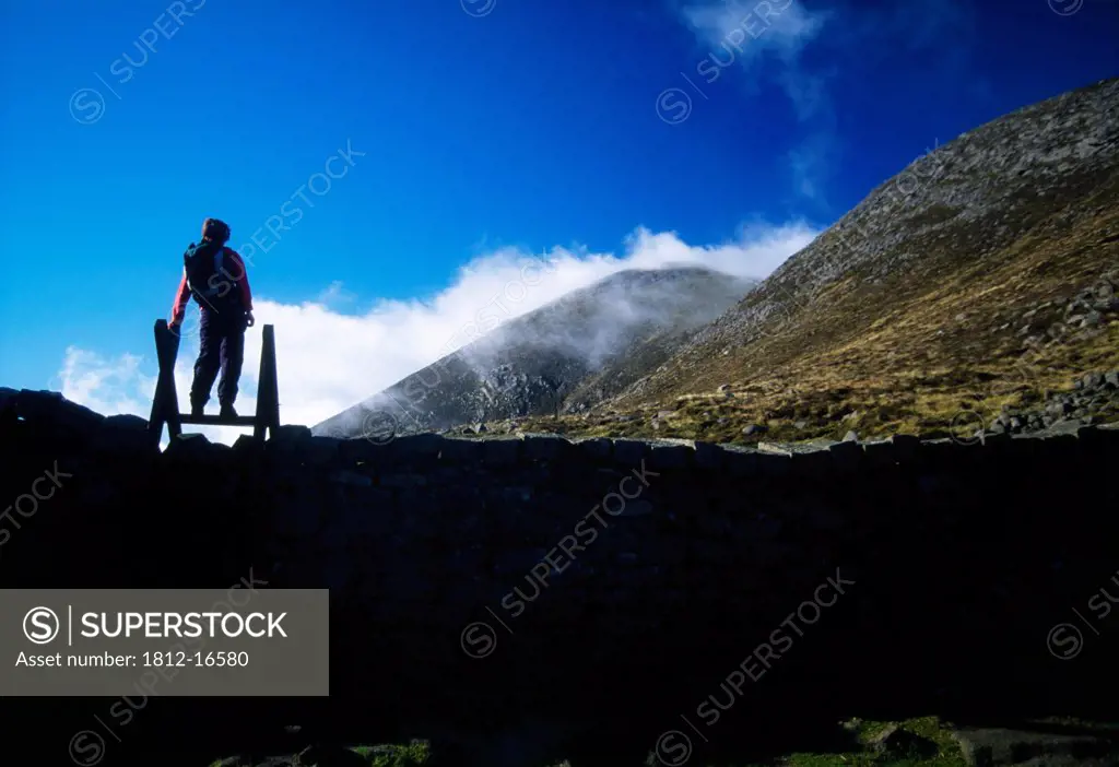 Mourne Wall, Slieve Meelbeg, Mountains Of Mourne, County Down, Ireland; Person Atop Stone Wall Viewing Mountain Range