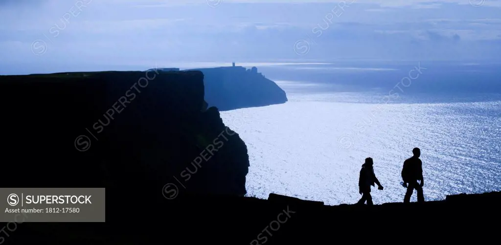 Cliffs Of Moher, County Clare, Ireland; Silhouette Of Hikers On Coastal Cliff