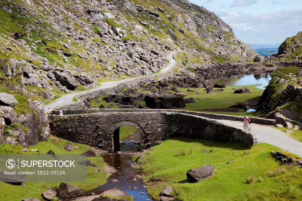 Riding A Bike On The Road Over A Bridge; Gap Of Dunloe, County Kerry, Ireland