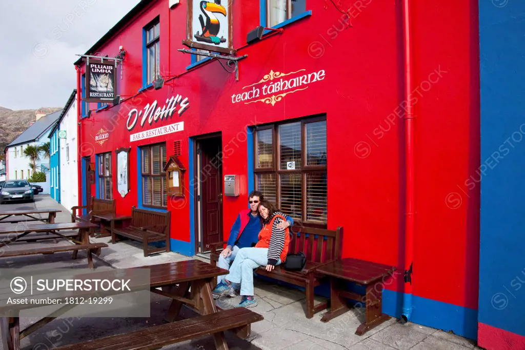 A Couple Sits On A Bench Outside O'neill's Pub; Allihies, County Cork, Ireland
