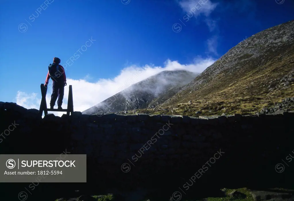 Mourne Wall, Slieve Meelbeg, Mountains of Mourne, County Down, Ireland; Person atop stone wall viewing mountain range