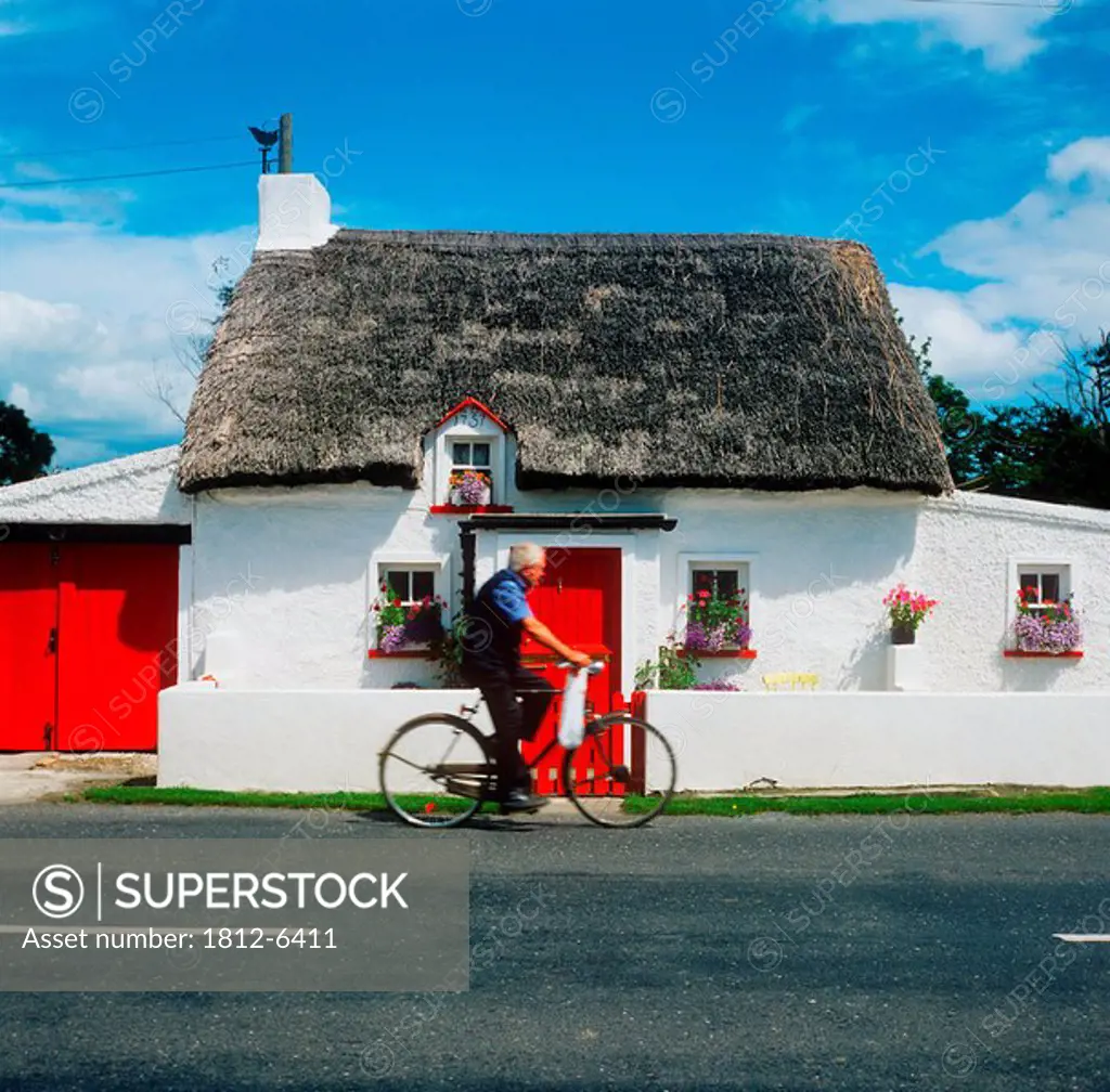 Side profile of a man riding a bicycle in front of a cottage, Mooncoin, County Kilkenny, Republic Of Ireland