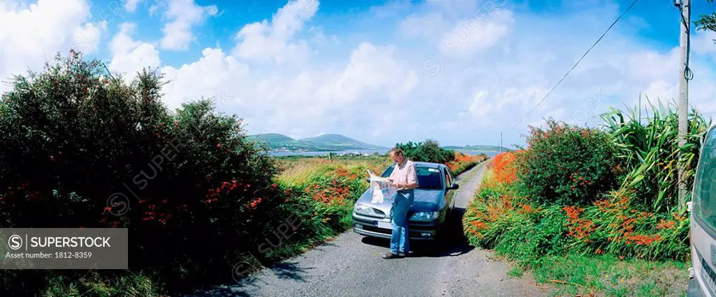 Cahirciveen, Co Kerry, Ireland, Man standing by his car on a country road