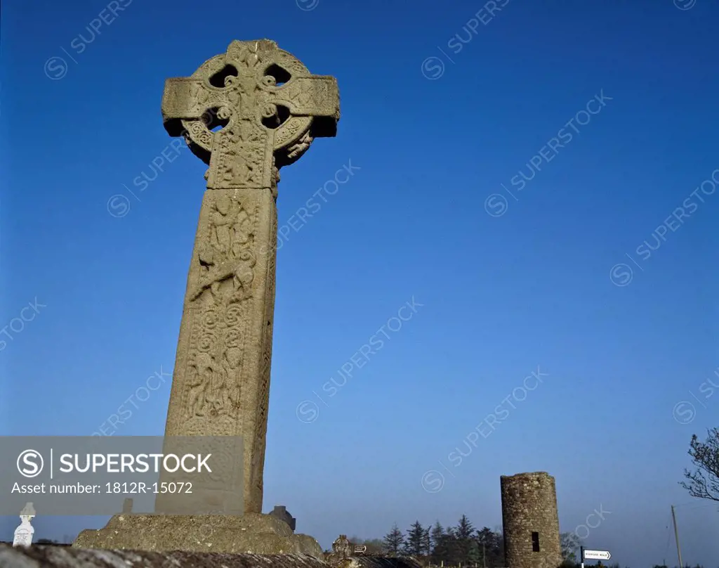 Celtic Cross In A Burial Ground With A Round Tower In The Background