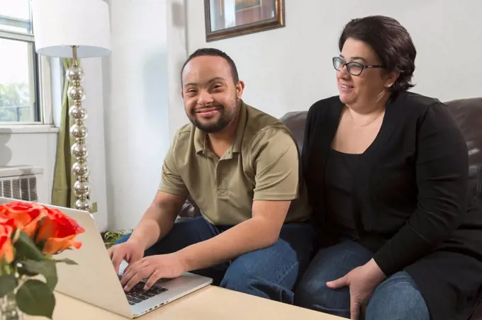 African American man with Down Syndrome using a laptop with his mother at home