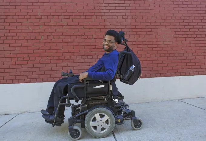Happy African American man with Cerebral Palsy using his power wheelchair outside