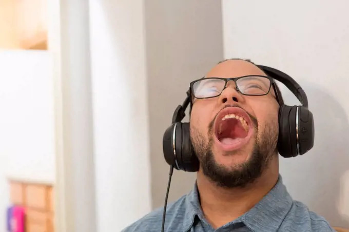 Happy African American man with Down Syndrome listening to music and singing with headphones at home