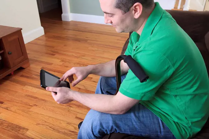 Man after anterior cruciate ligament (ACL) surgery with cane and using an digital tablet at home
