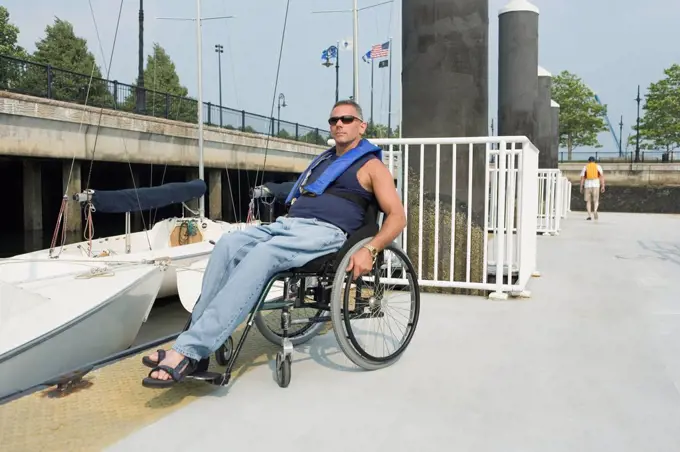 Mature man sitting in a wheelchair at a harbor for adaptive sailing