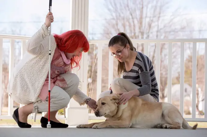 Two women with visual impairments, one with a service dog and one with a cane