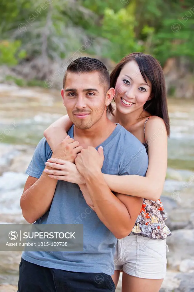 USA, Texas, Leakey, Young couple embracing at river bank, smiling, portrait