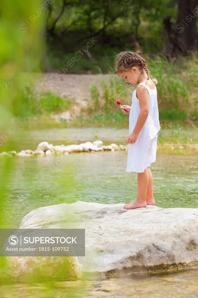 USA, Texas, Girl holding lollipop and standing on rock at Frio River