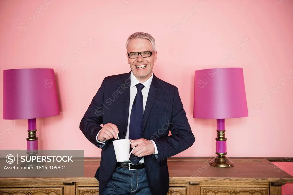 Germany, Stuttgart, Businessman stirring in cup, smiling, portrait